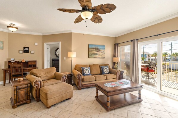 A living room with a ceiling fan, a sofa set, a coffee table, and a dining area with a view of the outdoors. - Beautiful Condo with Hot Tub & Pool - Walk to Beach, Snowbirds Welcome (Mexico Beach)