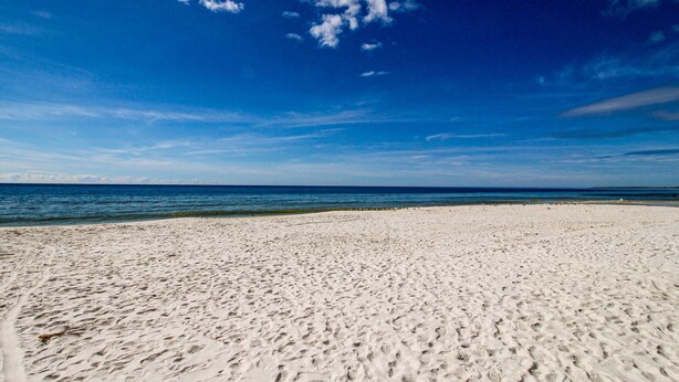A wide sandy beach with a clear blue sky and ocean in the background.