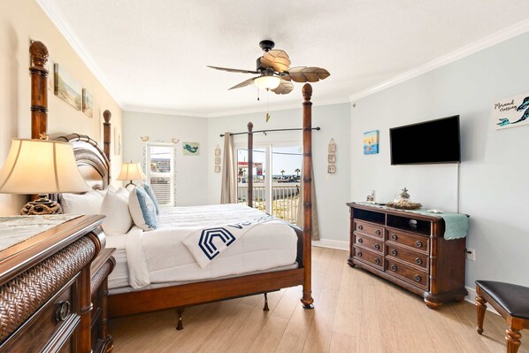 A bedroom with a four-poster bed, a ceiling fan, a dresser, and a television on the wall.