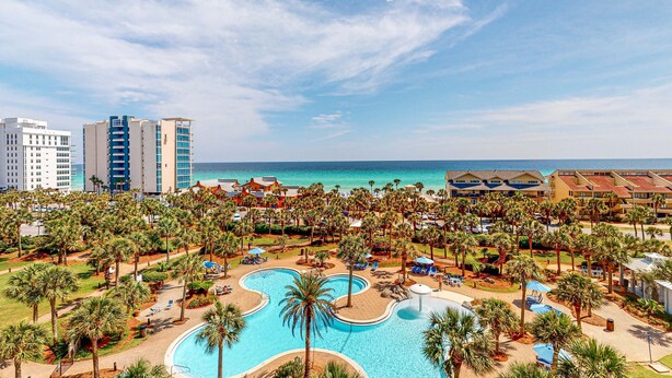 Ein Resort mit einem großen Schwimmbad, Palmen und Blick auf den Strand.