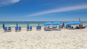 Ein Strand mit blauen Liegestühlen und Sonnenschirmen, einem klaren Himmel und dem Ozean im Hintergrund.