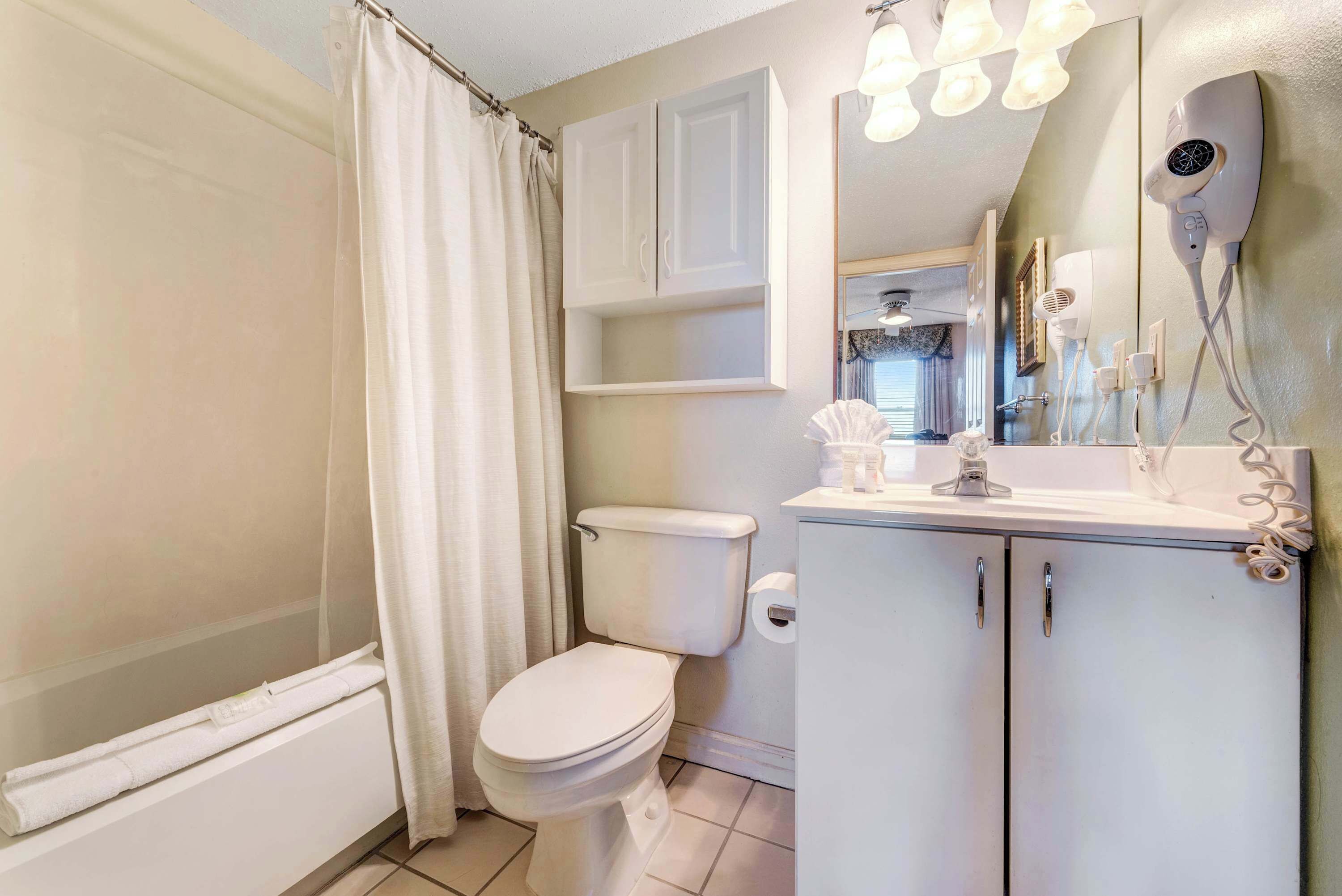 A bathroom with a toilet, a shower curtain, a cabinet, and a hairdryer mounted on the wall.