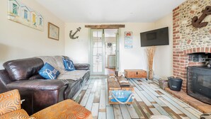 Ein Wohnzimmer mit einer Ledersofa, gemusterten Kissen, einem Holztisch, einem Kamin aus Stein und einem an der Wand befestigten Fernseher.