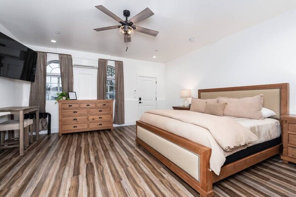 A bedroom with a bed, wooden dresser, desk, and a ceiling fan.