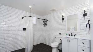 A modern bathroom with white subway tiles, a white toilet, a black shower curtain, and a white sink with a mirror above it. - Exquisite Chic King Suite at Yosemite`s Doorstep (Oakhurst)