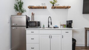 A modern kitchen with white cabinets, a stainless steel refrigerator, a microwave, a coffee maker, and wooden shelves above the counter. - Exquisite Chic King Suite at Yosemite`s Doorstep (Oakhurst)