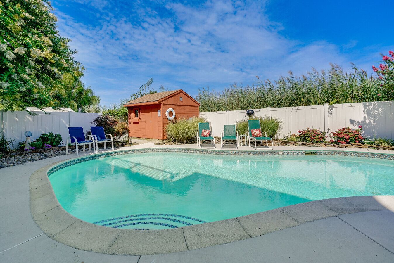 Une piscine avec un petit abri, des chaises longues et une clôture blanche.