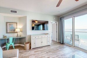 Ein geräumiges Zimmer mit einem großen Schiebeglastür, die auf einen Balkon führt, einem Holzboden, einer weißen Kommode, einem blaugrünen Sessel und einem gerahmten Bild an der Wand.