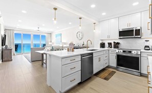 A modern kitchen with white cabinetry, stainless steel appliances, and a large island. - Scenic condo with balcony, beach access, pool & hot tub (Destin)