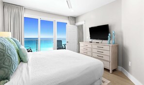 A bedroom with a large bed, a TV, a desk, and a view of the ocean. - Scenic condo with balcony, beach access, pool & hot tub (Destin)