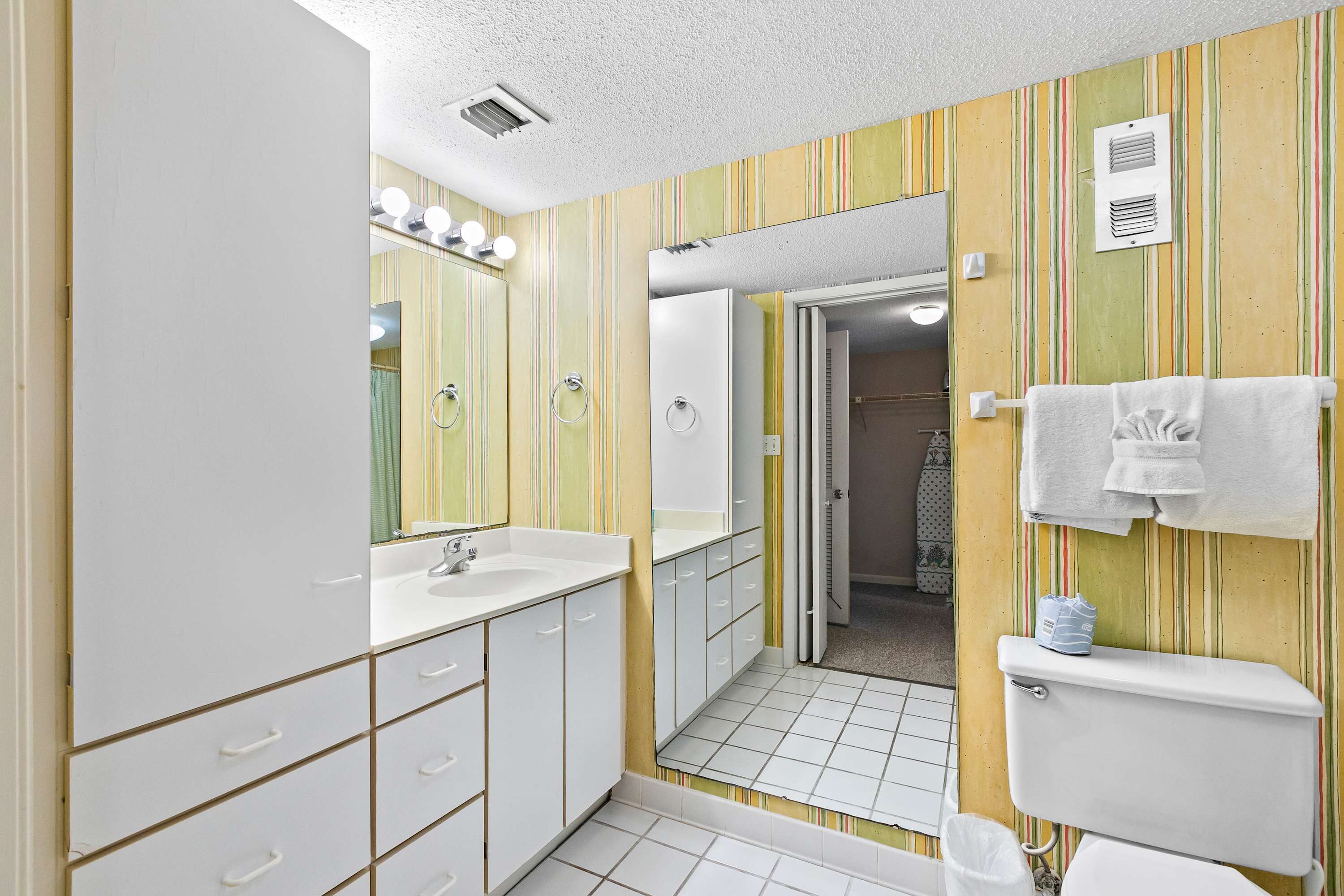 Een badkamer met een wit wastafelmeubel, spiegel en toilet, behang met strepen en een handdoekhouder.
