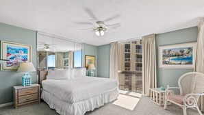 Ein Hotelzimmer mit einem großen Bett, einem Deckenventilator, einem Vorhangfenster, einem Sessel und einem kleinen Tisch.