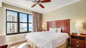 Hotellihuone, jossa on suuri sänky, puinen pääty, yöpöytä lampulla, ikkuna verhoilla ja näkymä rakennuksiin.