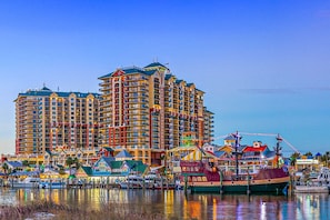 Um hotel à beira-mar com várias varandas, uma marina com barcos e diversos edifícios coloridos ao longo da costa.