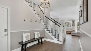 A modern interior with a staircase, a bench, and a chandelier. - Happy Hours (Destin)