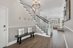 A modern interior with a staircase, a bench, and a chandelier. - Happy Hours (Destin)