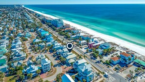 An aerial view of a coastal town with a beachfront, featuring a mix of residential and commercial buildings, roads, and a clear view of the ocean. - Happy Hours (Destin)