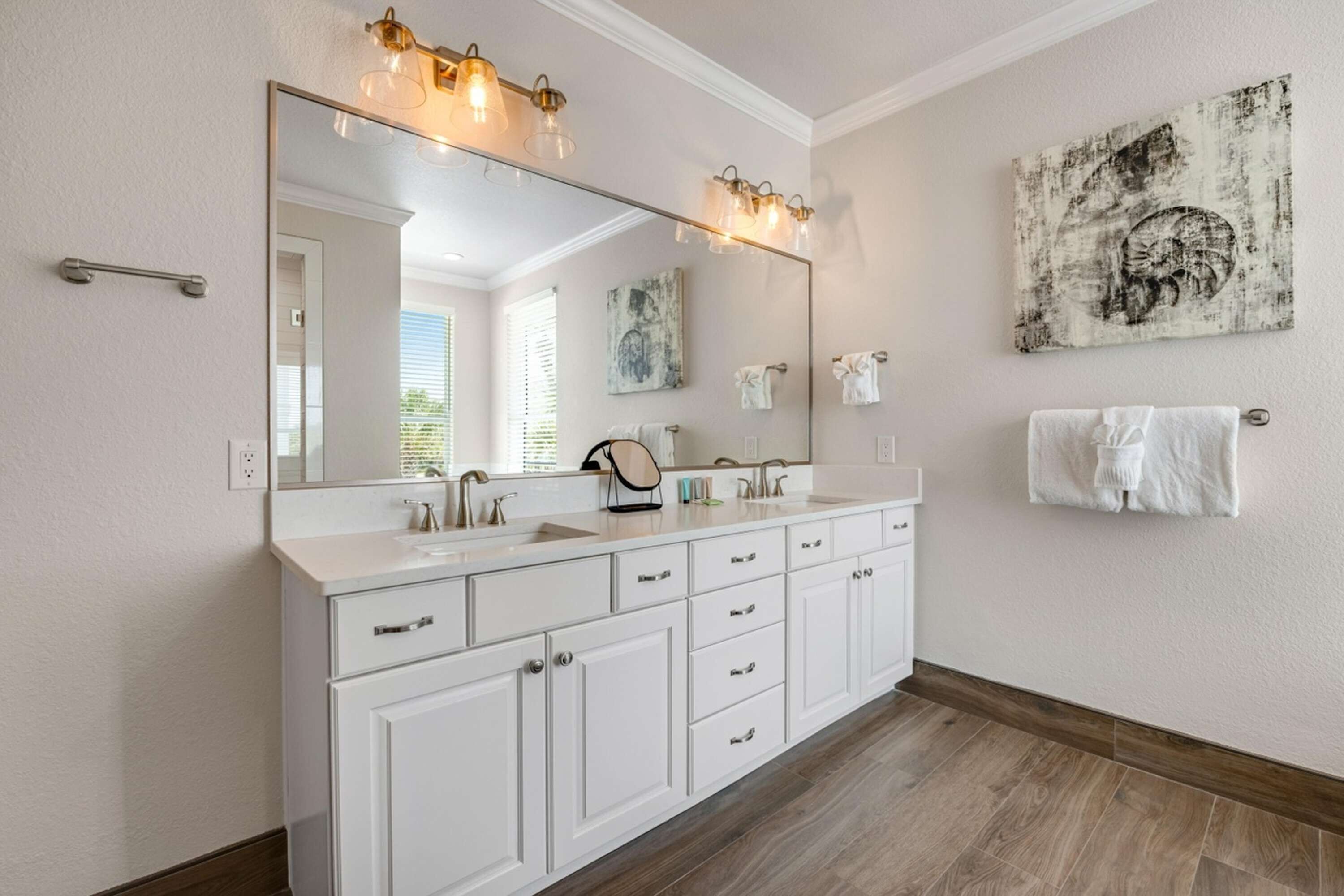 A bathroom with a large mirror, white cabinets, a double sink, and a towel rack.