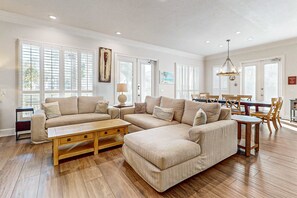 Amplia sala de estar con un sofá seccional grande, una mesa de centro de madera y un comedor con sillas de madera.