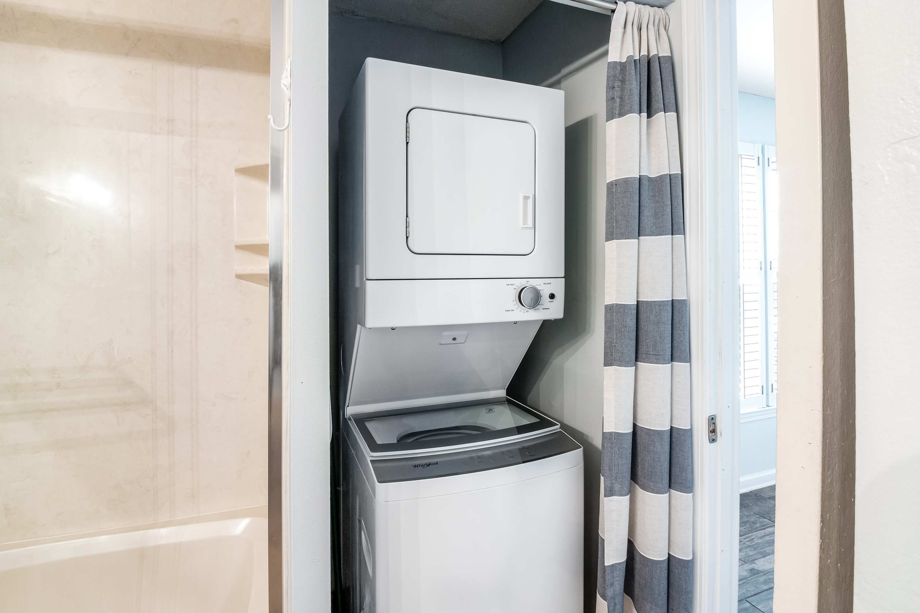 A compact laundry room with a front-loading washer and dryer, a striped curtain, and a tiled floor.