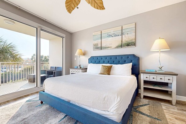 A bedroom with a large bed, two bedside tables, a balcony with a view, and a beach-themed wall art piece. - Romantic beachfront getaway with pool, gym, private balcony & washer & dryer (Destin)