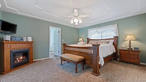 Ein Schlafzimmer mit Kamin, einem Bett, einer Bank, einem Nachttisch, einer Lampe und einem Deckenventilator.