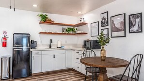 Una cucina moderna con mobili bianchi, un frigorifero nero, un tavolo da pranzo in legno con due sedie e un estintore a parete.