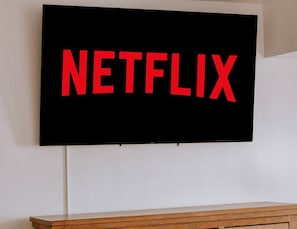 Un téléviseur à écran plat fixé au mur, avec le mot « NETFLIX » affiché en lettres rouges.