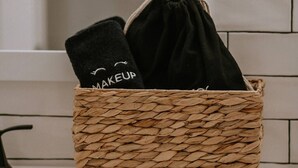 Un cesto intrecciato con una sacca nera con coulisse e un asciugamano nero con la scritta 'MAKEUP'.