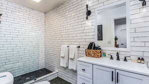 Un bagno con piastrelle bianche a metro, pavimento nero esagonale, water bianco, lavandino bianco con rubinetto nero e mobile contenitore bianco con cassetti.