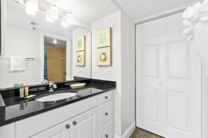 A bathroom with a black countertop sink, white cabinets, and a large mirror. There are framed pictures on the wall and a towel rack with a white towel. - 10th Floor Beautiful Condo, Splash pad w multiple pools & hot tub (Destin)