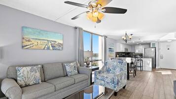 Ein modernes Wohnzimmer mit einem grauen Sofa, einem gemusterten Sessel und einem Deckenventilator.