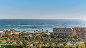 A coastal hotel with a view of the ocean, featuring a parking lot, palm trees, and multiple buildings. - Captiva beachfront condo w ocean views and pool & fitness center access (Destin)