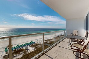 Ein Balkon mit Glasgeländer, der auf einen Strand mit Sonnenschirmen und einem klaren Himmel blickt.
