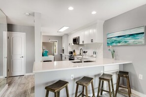 Une cuisine moderne avec des meubles blancs, un grand îlot central doté de tabourets et un tableau accroché au mur.