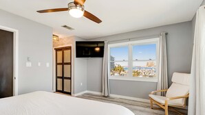 Ein Schlafzimmer mit einem Bett, Deckenventilator, Fernseher, Fenster mit Blick und einem Sessel.