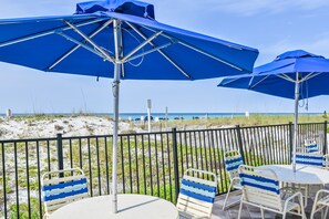 Outdoor seating with blue umbrellas, a view of the beach, and a fence. - Beachfront, 15th-floor condo with great Gulf view, hot tub, pools & gyms (Destin)