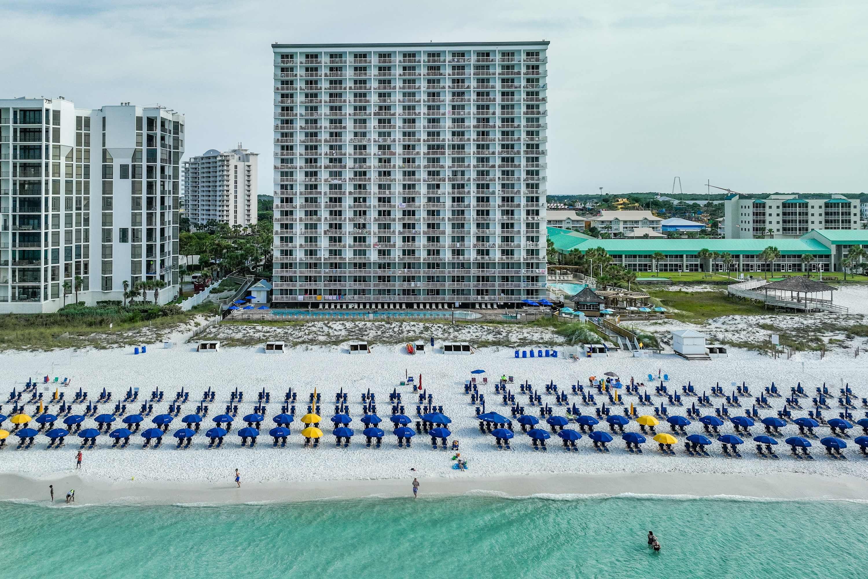 Een strandhotel met een groot gebouw, een zandstrand met parasols en een helder uitzicht op de oceaan.