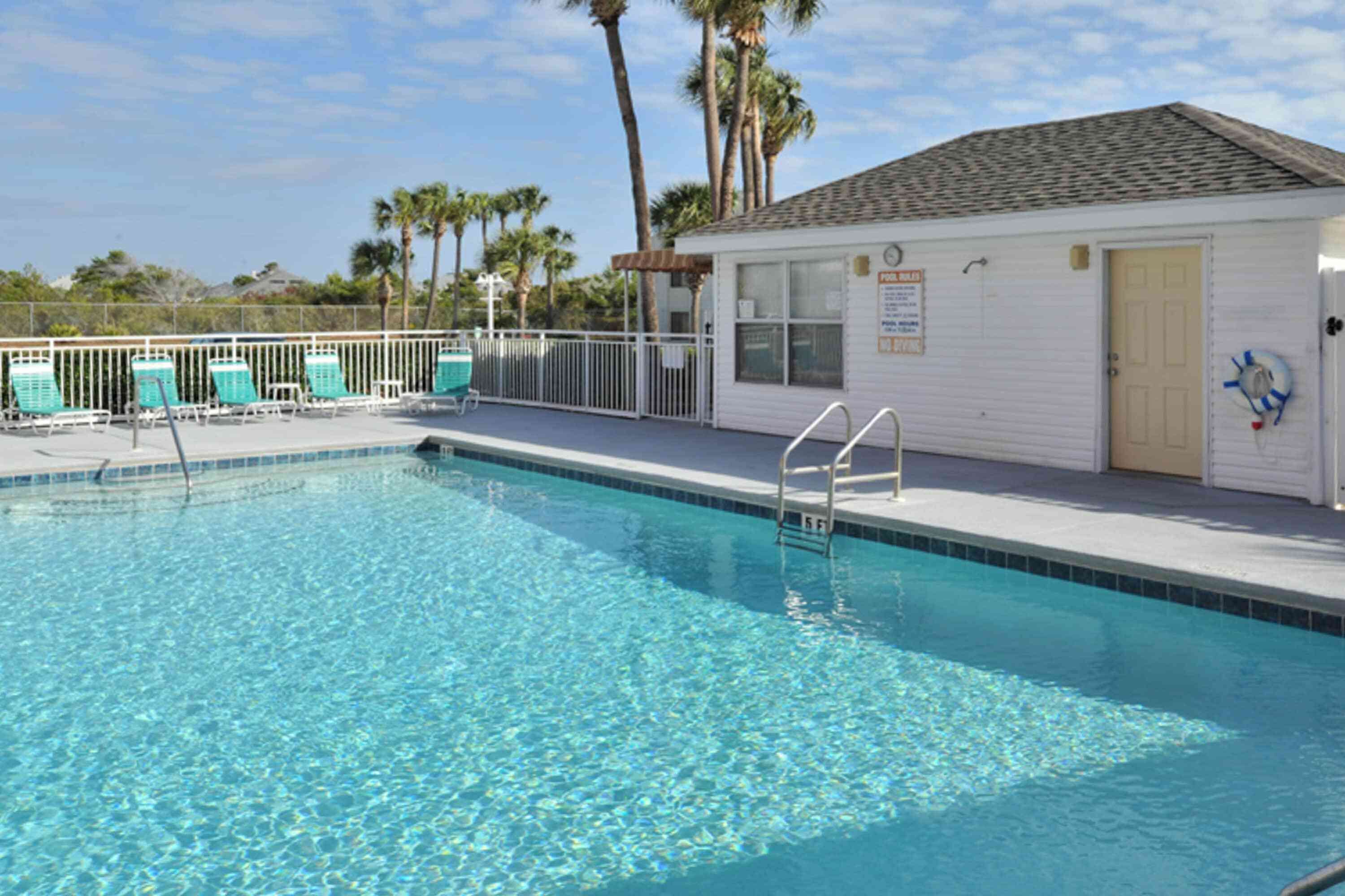 A swimming pool with a lifeguard stand, a small building with a door, and a fenced area with lounge chairs.