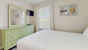 Un dormitorio con cama, cómoda, espejo, televisor y ventana con cortinas.