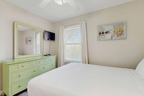 A bedroom with a bed, a dresser, a mirror, a television, and a window with curtains. - Bright, coastal condo with resort pool and hot tub (Miramar Beach)