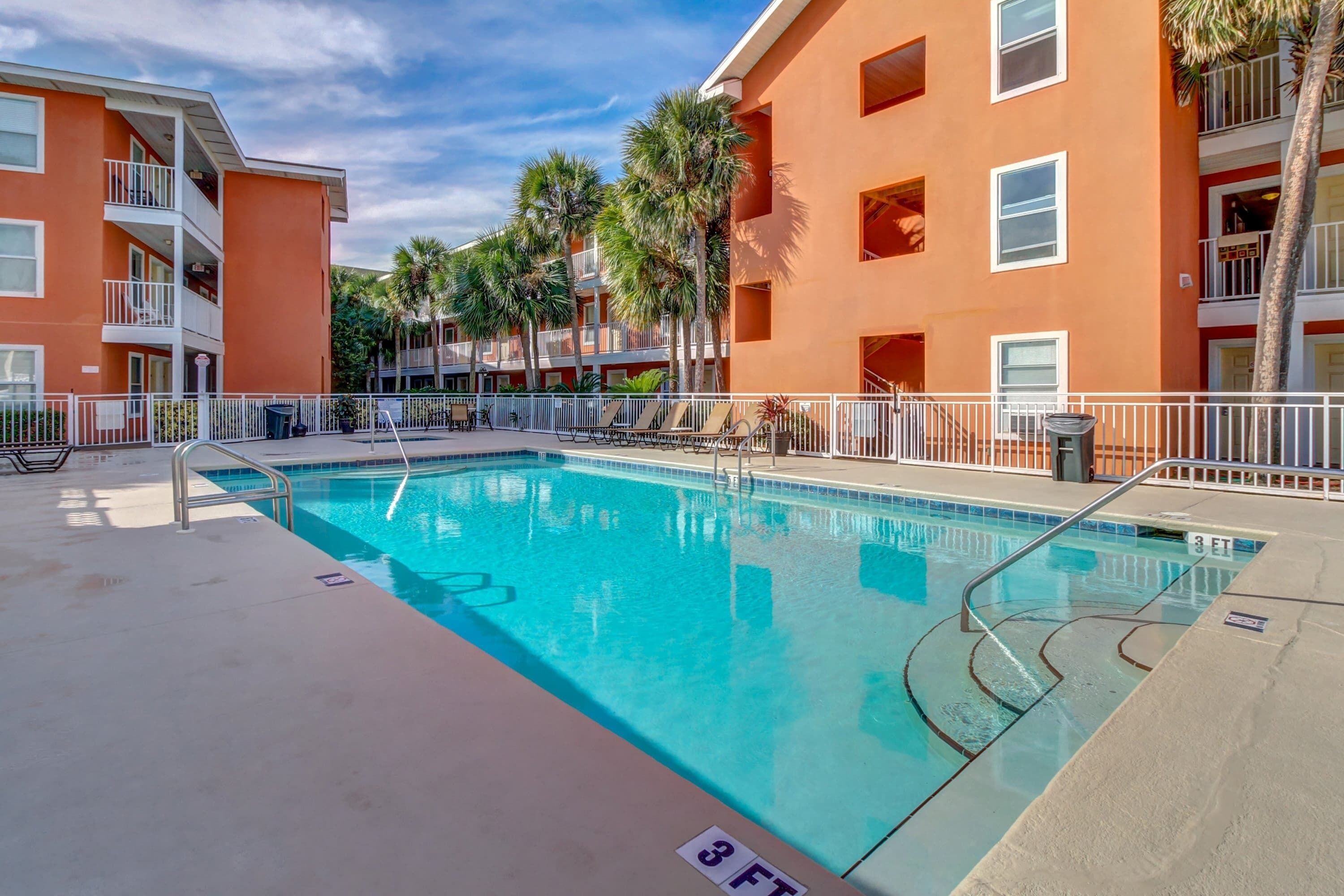 Una piscina interior con indicador de profundidad de 3 pies, rodeada de edificios color naranja con balcones y palmeras.