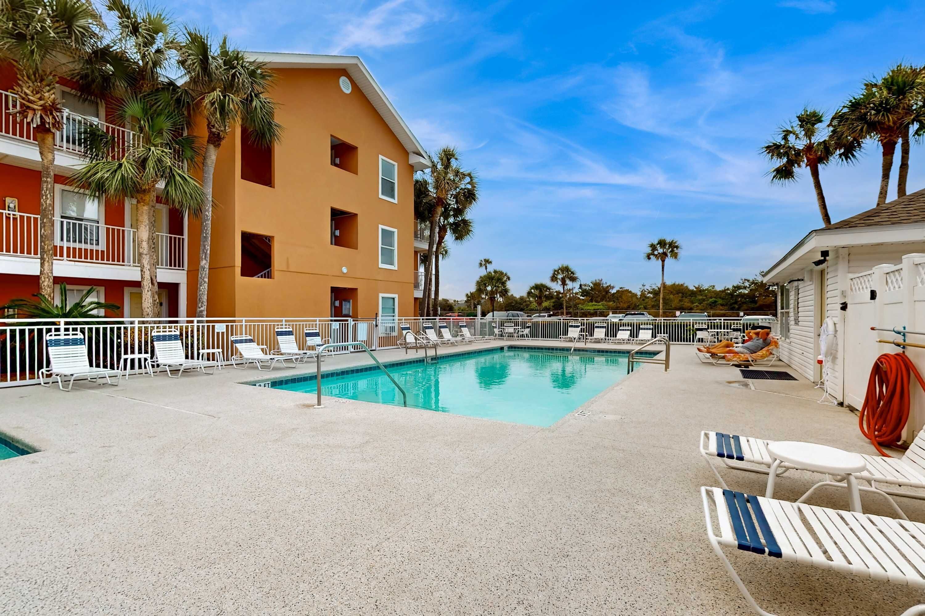 A pool area with lounge chairs, a pool, and a building with balconies.