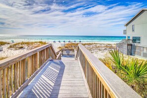 A wooden boardwalk leading to a beach with a building on the right. - Cozy coastal condo with patio, shared pool & beach access (Miramar Beach)