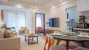 A modern living room with a sofa, coffee table, dining table, chairs, a TV, and a kitchen area with a coffee machine. - Modern JW 1BR Westlands Nairobi homes with pool and gym (Nairobi)