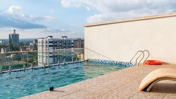A rooftop pool with a city view, a lounge chair, and a pool ladder. - Modern JW 1BR Westlands Nairobi homes with pool and gym (Nairobi)