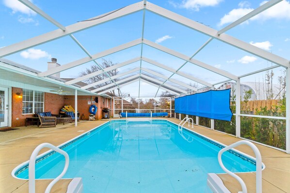 Ein Innenpool mit großen Glaswänden, eine überdachte Terrasse mit Liegestühlen und eine Backsteinwand.