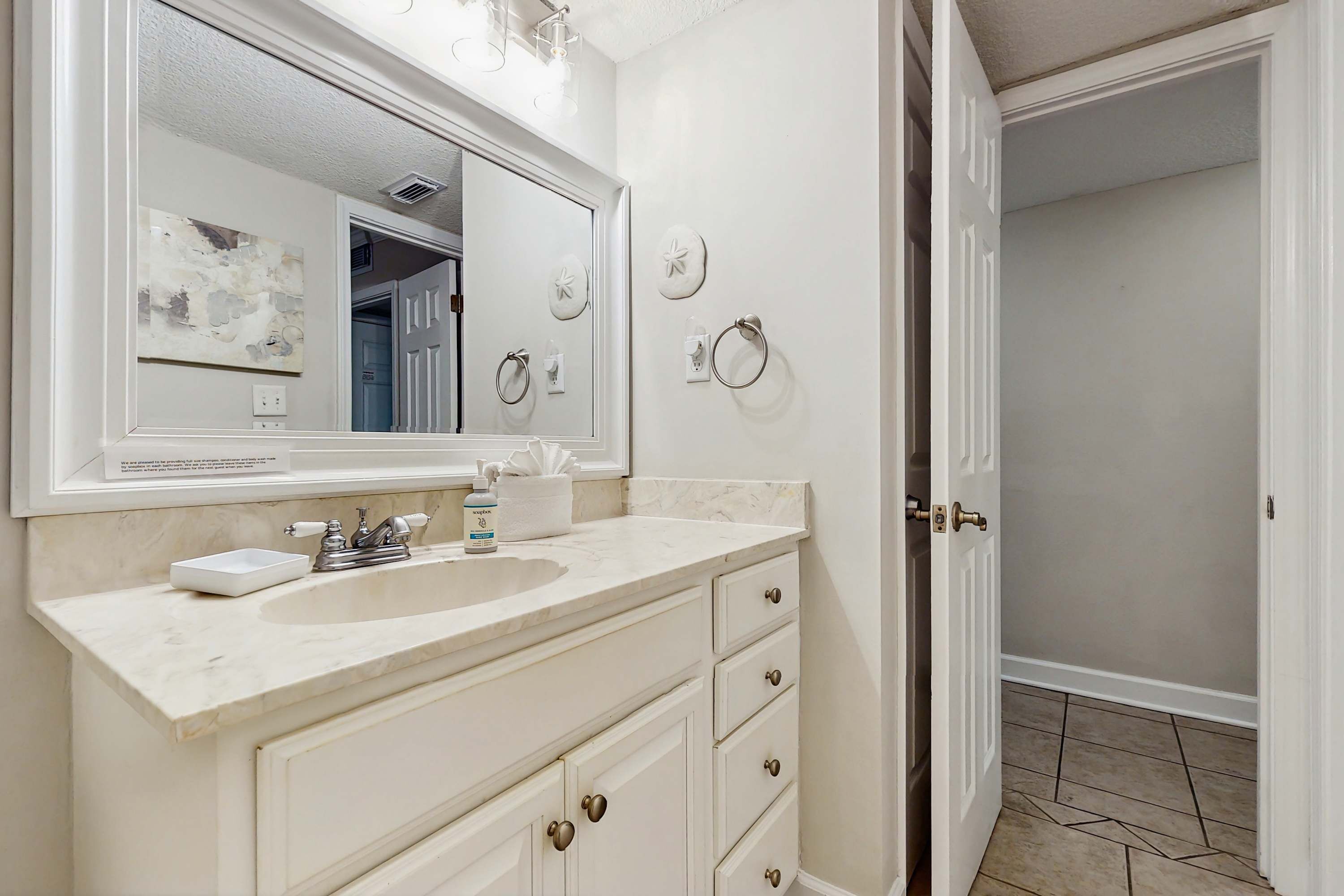 A bathroom with a white vanity, a large mirror, and a sink.