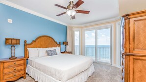 A bedroom with a large bed, wooden headboard, two bedside tables with lamps, a ceiling fan, and a view of the ocean through large windows. - Inviting Gulf-front condo In Perdido Key with waterfront pool/hot tub,oceanfront balcony & private cabana (Perdido Key)