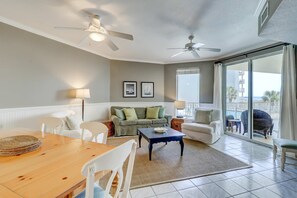 A spacious living room with a wooden dining table, white chairs, a sofa, and a balcony with a view of the ocean. - Two-bedroom with bunks, balcony overlooking pool & on-site pickleball (Santa Rosa Beach)
